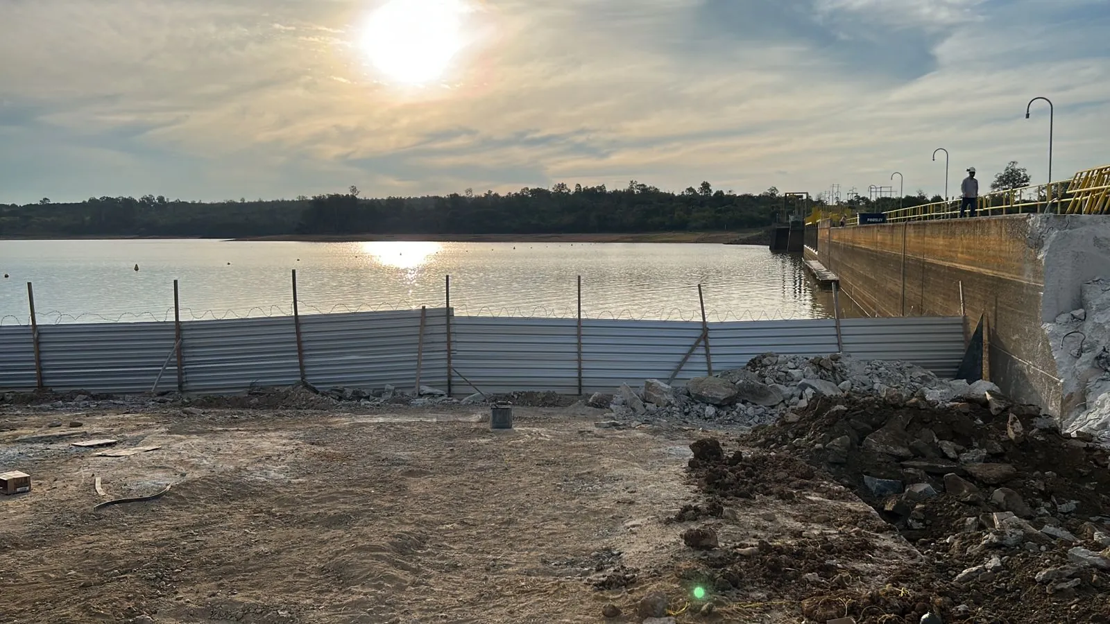 Frente de obra junto &agrave; barragem com cerca de prote&ccedil;&atilde;o e reservat&oacute;rio ao fundo
