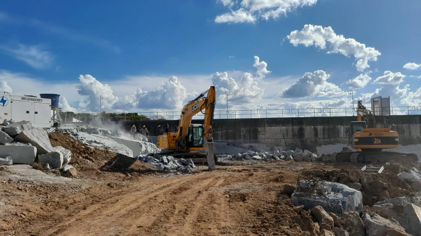 Escavadeira com martelete da Construtora Pizzane fragmentando rocha junto &agrave; barragem