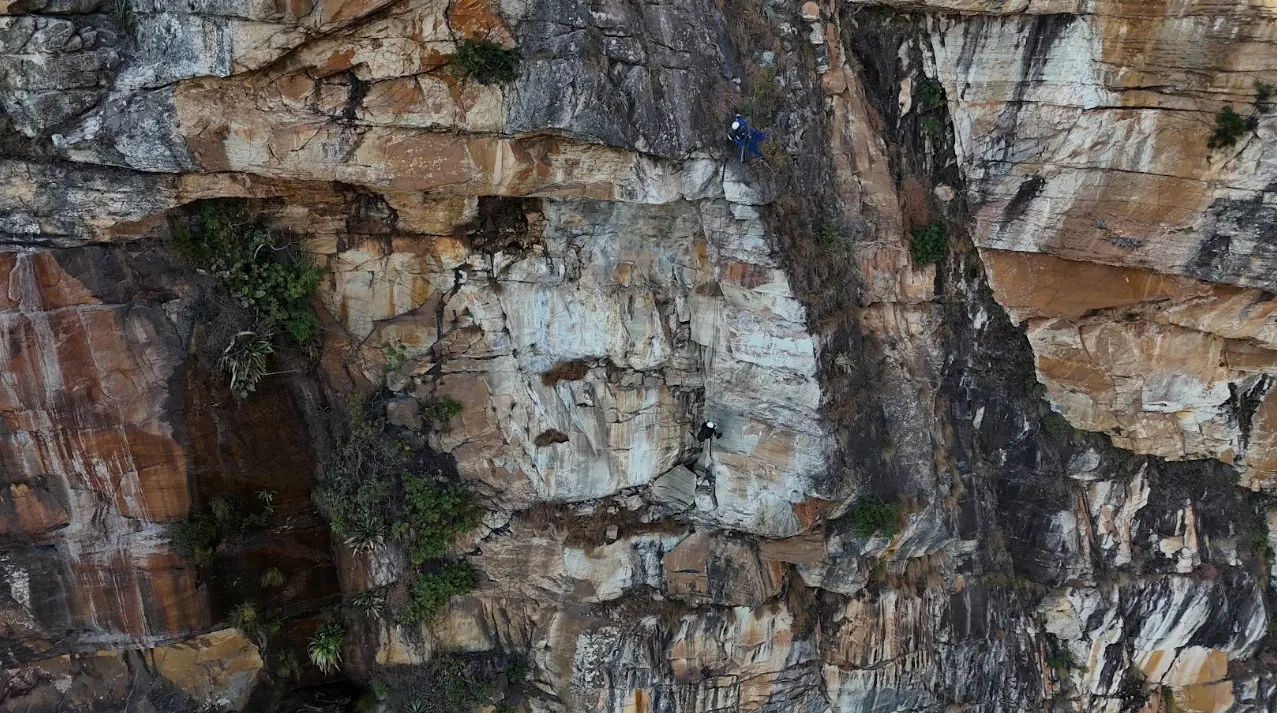 Alpinista industrial em rapel no paredão, mostrando a escala da parede rochosa